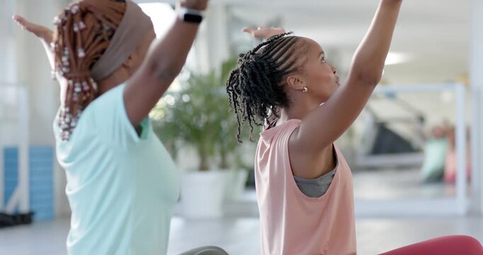 Two women after cue turning head opening chest and reaching overhead in guided stretch near mirror