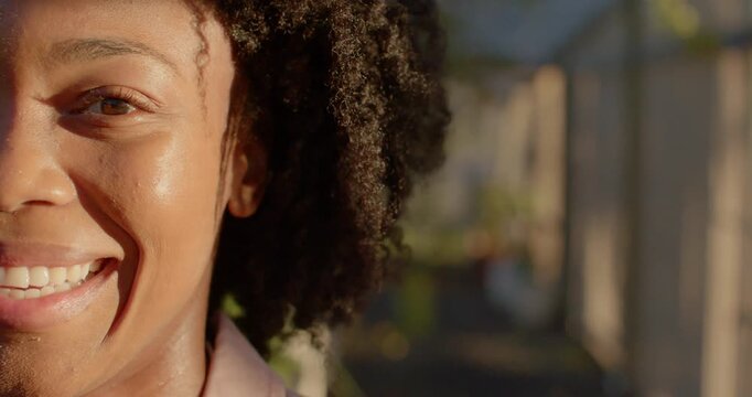 Mid-adult woman smiling, reacting to operator cue on sunlit path in collared top near fence plants