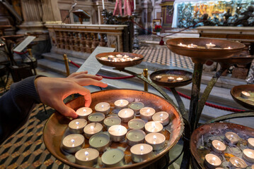 Naples, italy. December 27, 2024. Person's hand placing a lit votive tea light candle into a copper basin, praying for faith and devotion inside the cathedral of the assumption of mary