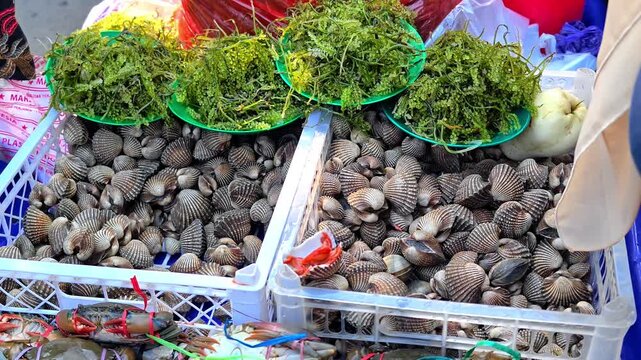 Fresh clams and seaweed are sold at a traditional seafood market, with sellers and buyers engaged in transactions. An authentic local market scene showcasing fresh seafood and daily trade.