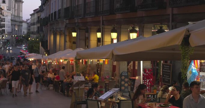 Madrid, Spain, July 4, 2026: Evening outdoor dining along Plaza Mayor with restaurants, pedestrians and warm street lighting. Historic arcades create a lively urban atmosphere.