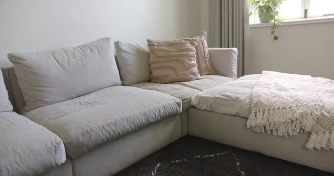 Light-beige L-shaped sofa is getting daylight from curtained window, creating subtle shadow shifts