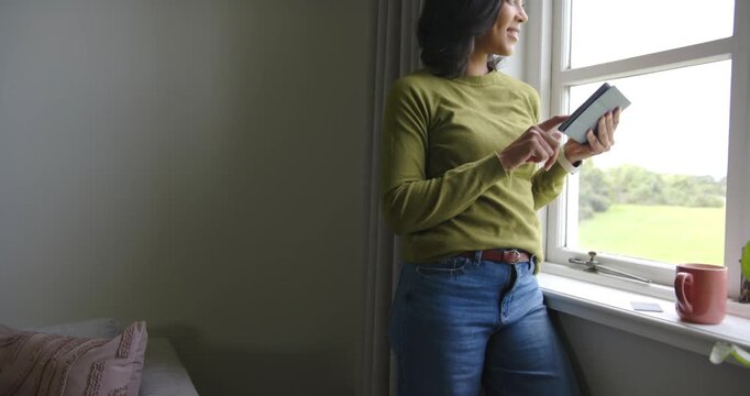 African American woman entering from right leaning on sill using tablet looking outside, copy space