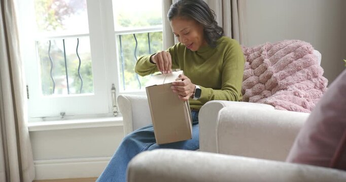 African American woman inspecting taped top, peeling tape and checking box contents in living room