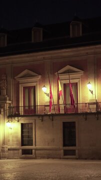 Madrid, Spain, July 4, 2026: Illuminated facade of the historic Casa de la Villa at night. Spanish and Community of Madrid flags hang from the balcony while warm street lighting highlights the histori