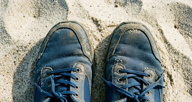 Vista da sopra in primo piano di vecchio e consunto  paio di scarpe sportive su una superficie di fine sabbia