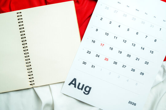 An August 2026 wall calendar page sitting beside an open, empty spiral-bound notebook on a textured background, ideal for planning, scheduling, or time management concepts