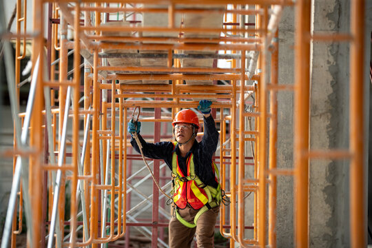 Construction worker skillfully maneuvering through scaffolding at a busy building site while equipped with essential safety gear and tools
