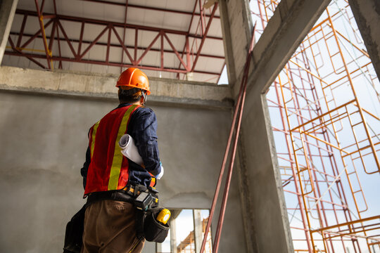 Construction engineer reviewing plans at a building site with safety gear and scaffolding in the background