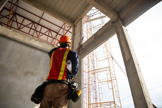 Construction engineer monitoring the progress of a building project while holding a blueprint on site