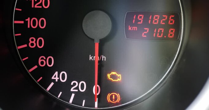 Car dashboard turning on with warning lights and odometer display as the engine starts up, close up of speedometer at zero