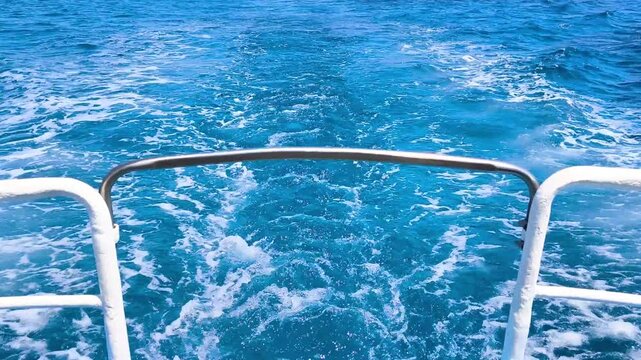 Foamy boat wake stretching across the blue ocean, viewed from the stern of a vessel. Summer travel concept featuring open sea, maritime transport, and leisure cruising.