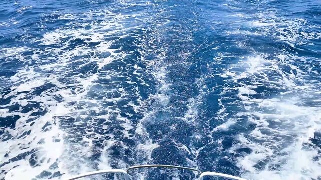 Boat stern with foamy wake on the deep blue sea during a sunny summer day. View from the deck of a moving vessel on open water, symbolizing travel, tourism, and marine adventure.
