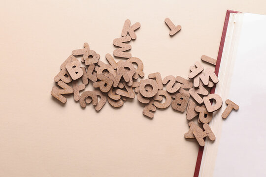 Book with many wooden letters on a beige background. Education, learning concept.
