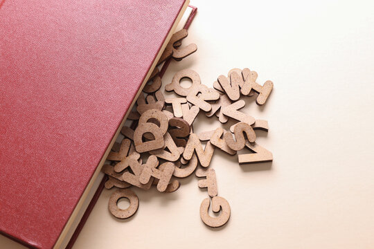 Book with many wooden letters on a beige background. Education, learning concept.