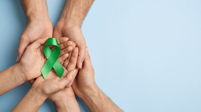 Top view of diverse hands cupped together holding a green ribbon symbolizing mental health awareness and support on a light blue background with copy space.
