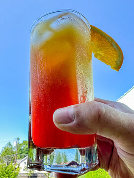 Hand holding cold cocktail with orange slice under blue sky