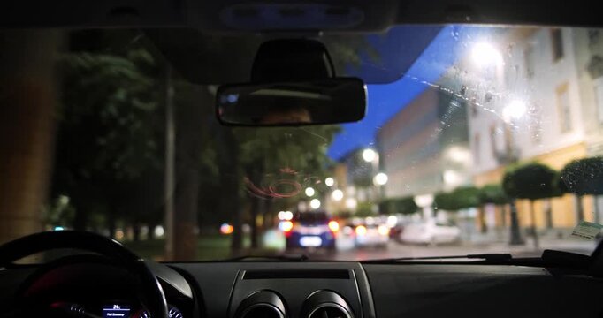 View from inside car driving on city street at night, dashboard and rearview mirror POV bokeh city lights