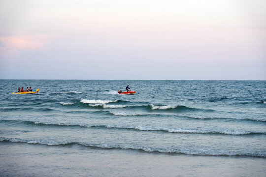 Scenic view of a calm ocean at sunset with small recreational boats or jet skis floating on the gentle waves.