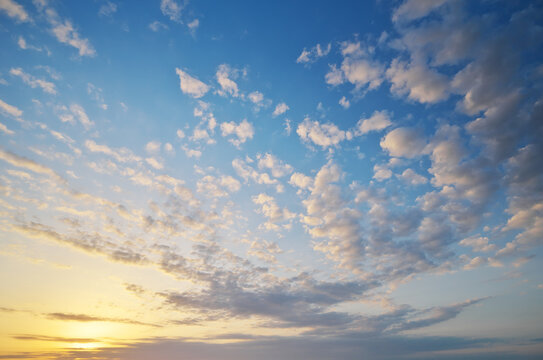 Blue sky background filled with scattered fluffy white and golden clouds at sunset.