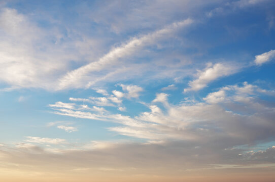 Blue sky background with soft white cirrus clouds and a warm pastel gradient at sunset.