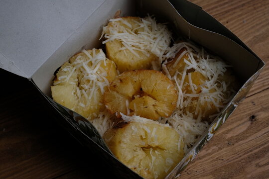 Fried Cheese Cassava with a crispy top of grated cheese and sweetened condensed milk in a paper box on a wooden table