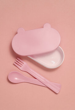Set of plastic dishes for feeding baby on pink background. Top view. Flat lay