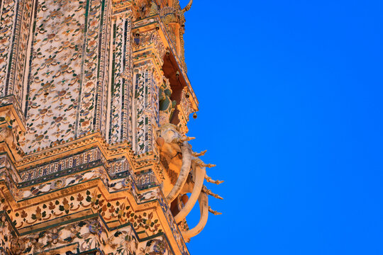 Fragment of the Phra Prang, the central tower of the Wat Arun (Temple of Dawn) in Bangkok, Thailand. Indra God on his three-headed elephant Erawan against blue sky. Encrusted with colored faience