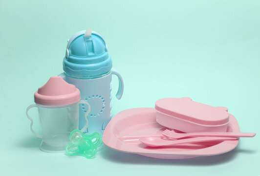 Set of plastic dishes for feeding baby and drinking bowls on blue background.