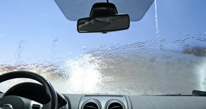 POV rinsing car windshield from inside cabin with pressure washer water spray