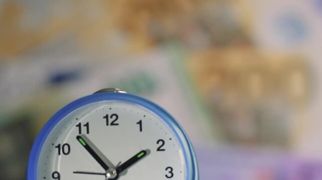 Alarm clock on a table surrounded by euro banknotes showing the time and currency details in a close-up shot