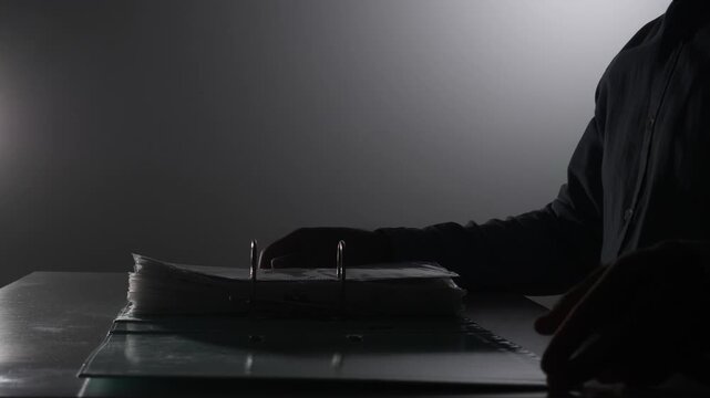 Person's hands, silhouetted in dramatic low light, carefully removing confidential files from a binder, symbolizing secrecy, investigation, and data theft in a clandestine operation