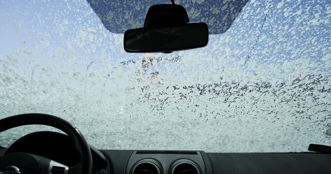 POV from inside a car looking through the windshield as a man sprays soap foam at a self-service car wash