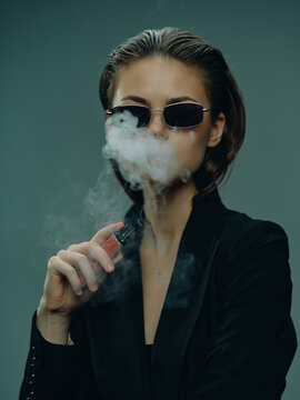 Woman wearing sunglasses vaping with smoke around her face in a dark moody setting