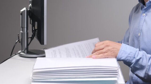 Person working in an office setting, reviewing sheets of corporate documents and files while simultaneously typing on a computer keyboard