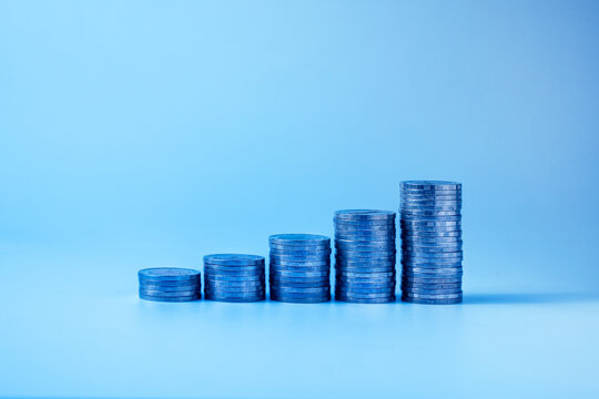 Stacked coins arranged in ascending order on a blue background, symbolizing financial growth, wealth accumulation, investment, savings, business success, and economic development. Minimal composition 