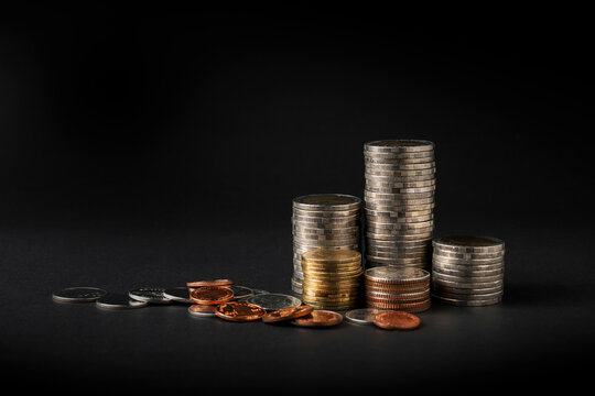 Stacks of assorted coins with scattered coins on a black background, symbolizing savings, investment, wealth accumulation, financial planning, and business growth. Minimal composition with dramatic li