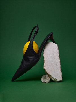 Black shoe with lemon on white rock against green