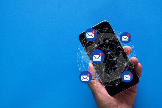 Top view of a hand holding a smartphone with floating unread email notification icons and a global network mesh on a blue background. Digital marketing, global communication,email newsletter concept