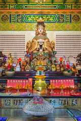 Obraz premium Ornate shrine with a large golden Mazu statue at Thean Hou Temple in Kuala Lumpur, Malaysia, featuring colorful offerings, fruit, and rows of miniature figurines on the temple wall