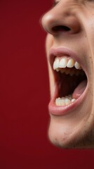 Fototapeta premium Close up of open mouth shouting against red background. Vertical photo of human teeth and tongue visible in wide open scream. Dental anatomy and vocal expression concept