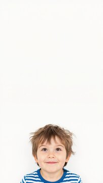 Young boy looking up at copy space on white background. Curious child in striped shirt with messy hair. Vertical portrait with blank space for text