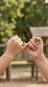 Vertical photo of children making pinky swear promise. Friendship and trust concept in playground setting. Close up of kids hands linked in promise gesture