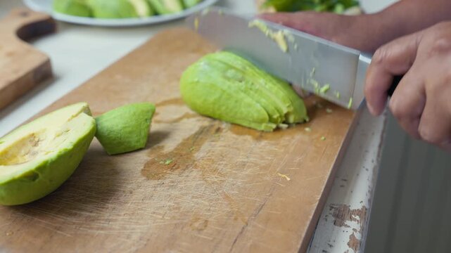 Slicing ripe avocado into thin wedges on a wooden cutting board.