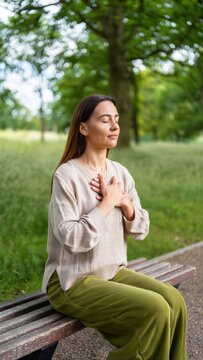 Seated woman on park bench with hands over heart, mindful breath awareness for vagal regulation, parasympathetic activation, emotional regulation, grounding practice, contemplative bond