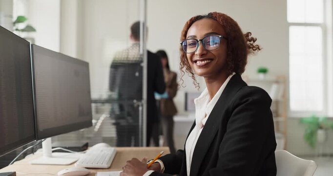 Businesswoman portrait smiling in office, computer analytics. The woman analyzes data and drives teamwork, refining reports and workflow with colleagues. Concept shows teamwork and analysis.