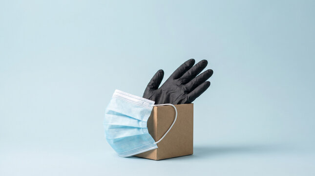 Cardboard box containing black rubber gloves with a blue surgical face mask attached on light blue
