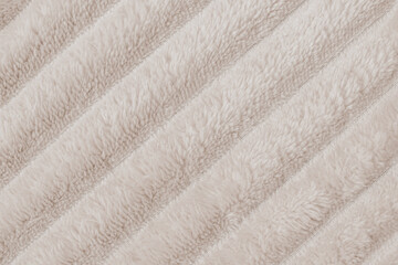 Horizontal close up flat lay shot of a cozy beige plush fleece blanket fabric texture with distinct diagonal ribbed rows of soft fluffy synthetic fur material © moryachka