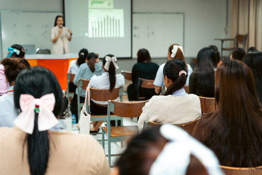 Female professor delivering an engaging academic lecture with crisp data charts on a projector screen to focused university students in a modern classroom