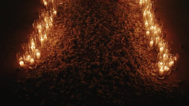 A magical wedding floor covered in thousands of rose petals and illuminated by dozens of candles in tall glass cylinders, creating a romantic and intimate path.